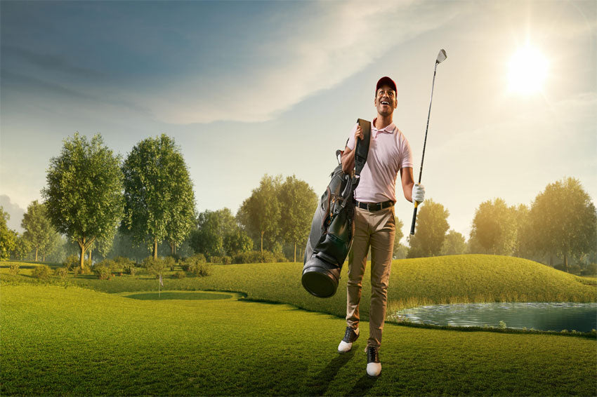 A guy walking in the golf field holding a Stinger Waterproof Bag